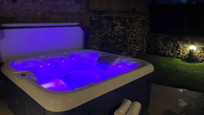 A hot tub with a stone wall backdrop, a stone fireplace, and a small grassy area. - Small Lane Barn (Stoke-on-Trent)