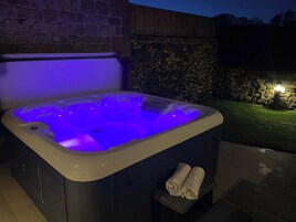Un jacuzzi con un fondo de pared de piedra, una chimenea de piedra y una pequeña zona cubierta de césped.