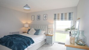 Ein Schlafzimmer mit einem Bett, Nachttischen, einer Heizung, einem Fenster mit Jalousien und Blick ins Freie.