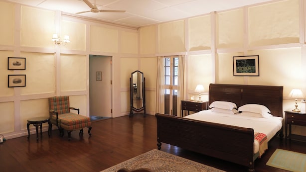 A spacious hotel room with a large bed, a chair, a mirror, and a ceiling fan.