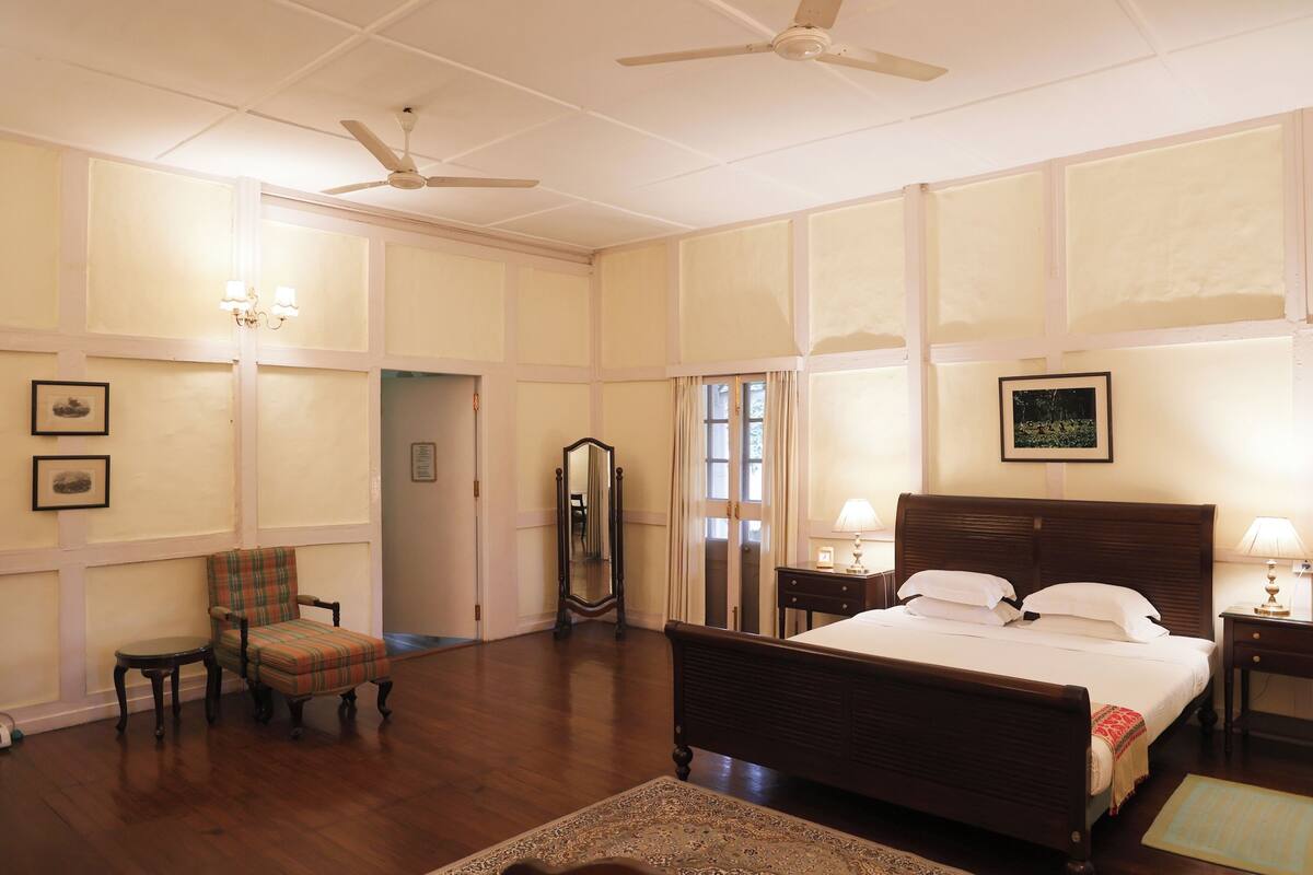 Um quarto de hotel espaçoso, com uma cama grande, uma cadeira, um espelho e um ventilador de teto.