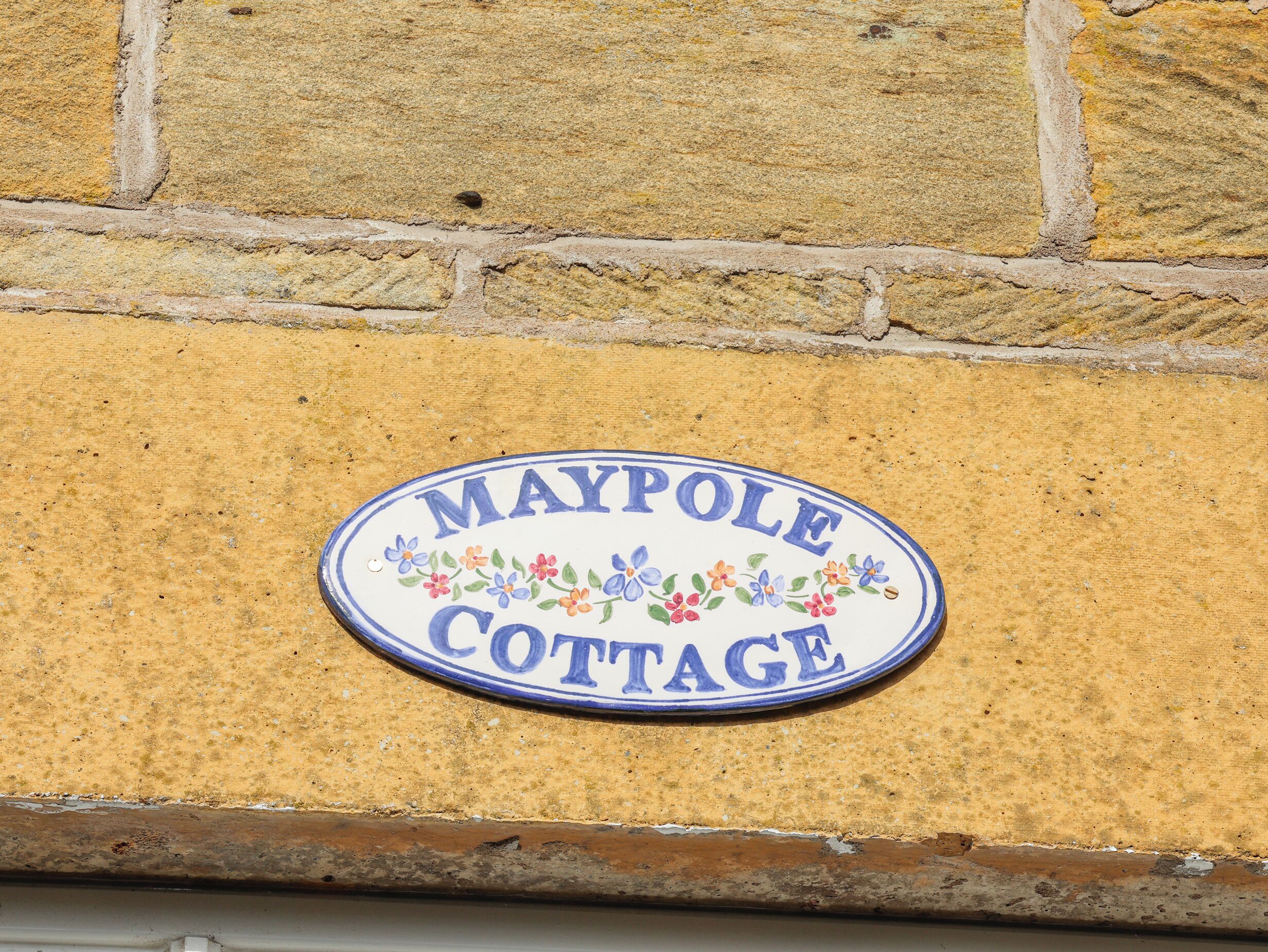 Una señal en una pared de ladrillo que dice 'Maypole Cottage'.