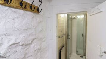 A bathroom with a glass shower door, white textured walls, and a wooden coat rack with black hooks.