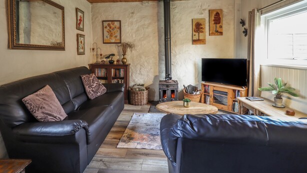 A cozy living room with a leather sofa, a television, a fireplace, and wooden ceiling beams.