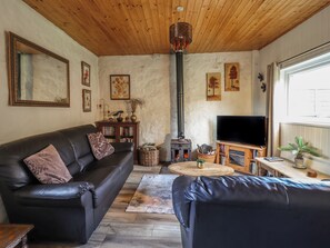 A cozy living room with a leather sofa, a television, a fireplace, and wooden ceiling beams. - Tyn Y Cefn (Blaenau Ffestiniog)