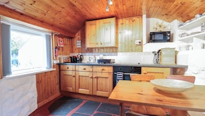 A wooden cabin kitchen with a dining area, including cabinets, a microwave, and a stove.
