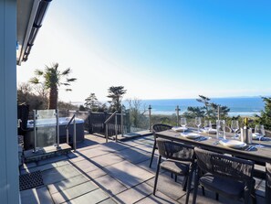 A patio with a table set for dining, overlooking a coastal view. - Aelfor (Harlech)