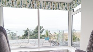 Una habitación con dos sillones tapizados en gris frente a un ventanal que da a un patio con plantas en macetas y vistas al océano.