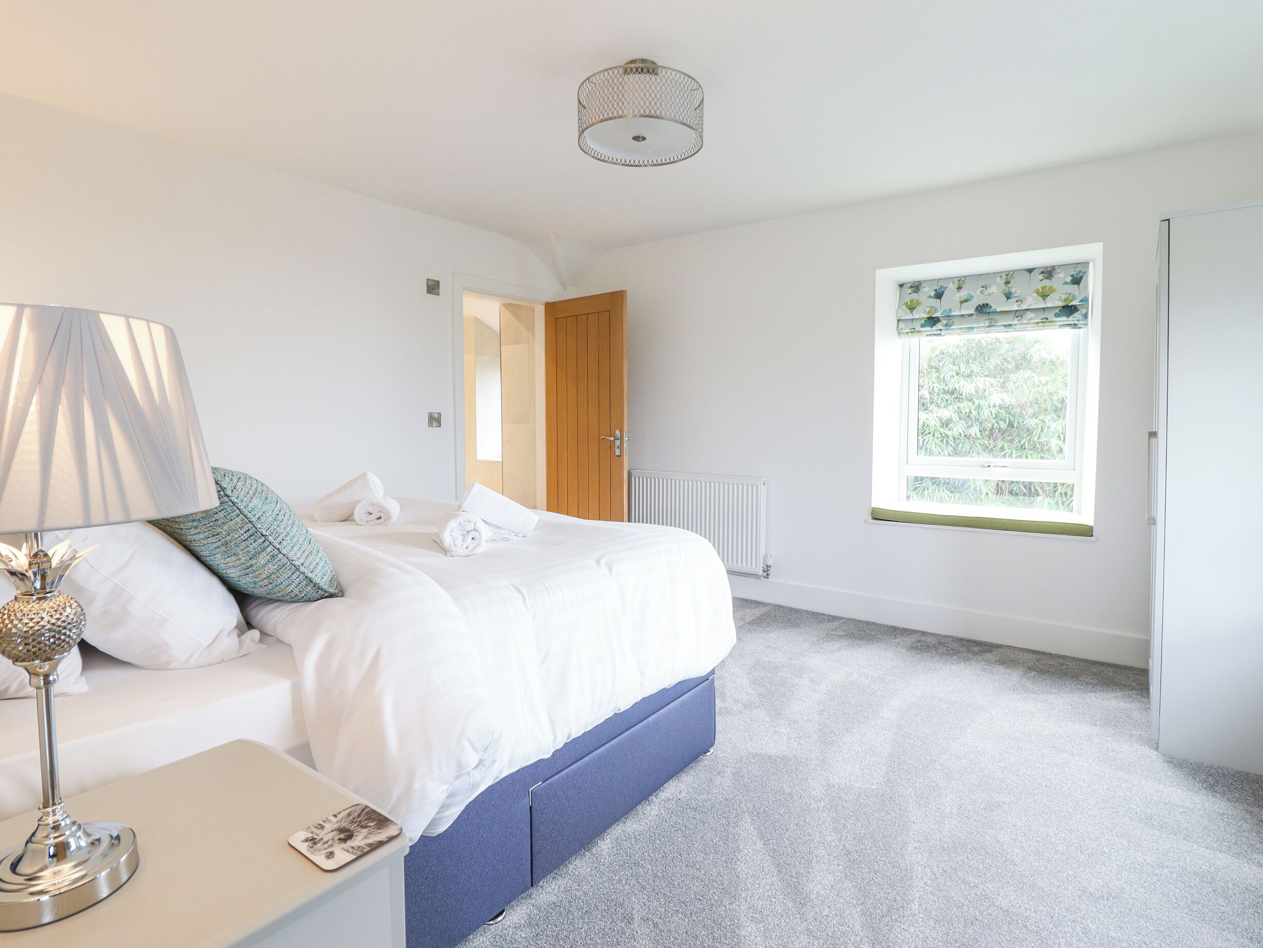 Une chambre à coucher avec un lit, une table de chevet avec une lampe, une fenêtre donnant sur un espace verdoyant et un radiateur.