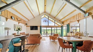 Une salle à manger spacieuse avec un haut plafond et de grandes fenêtres, des poutres en bois et une vue sur la campagne.