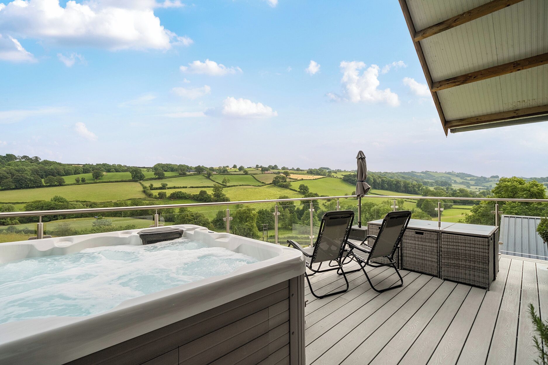 A hot tub on a deck with chairs and a view of green fields.