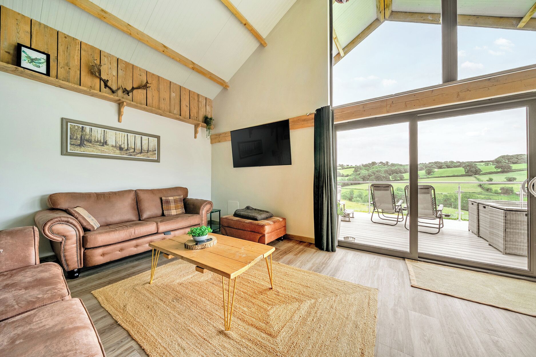 Una sala de estar con un sofá de cuero marrón, una mesa de centro de madera y un amplio ventanal corredera que da a una terraza exterior con sillas.