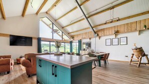 Une cuisine spacieuse dotée d’un grand îlot central, de poutres en bois et offrant une vue sur la campagne.