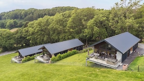 Un bâtiment moderne à deux étages, doté d’un toit plat, de grandes fenêtres et d’un espace extérieur aménagé avec des sièges.