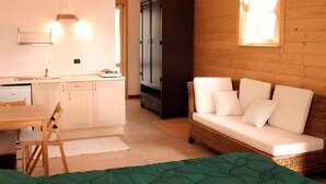 A cozy room with a green bed, a wicker sofa with white cushions, a wooden cabinet, and a small kitchenette. - Agriturismo Prisma: Double Room with Private Bathroom (Villa Vergano)