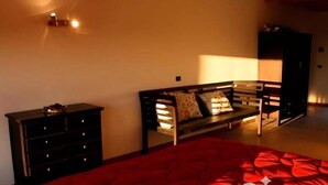 A bedroom with a red bedspread, a wooden bench, a dresser, and a lamp. - Agriturismo Prisma: Quadruple Room with Private Bathroom (Villa Vergano)
