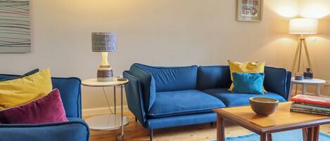 A living room with a blue sofa, a small round table, and a lamp.