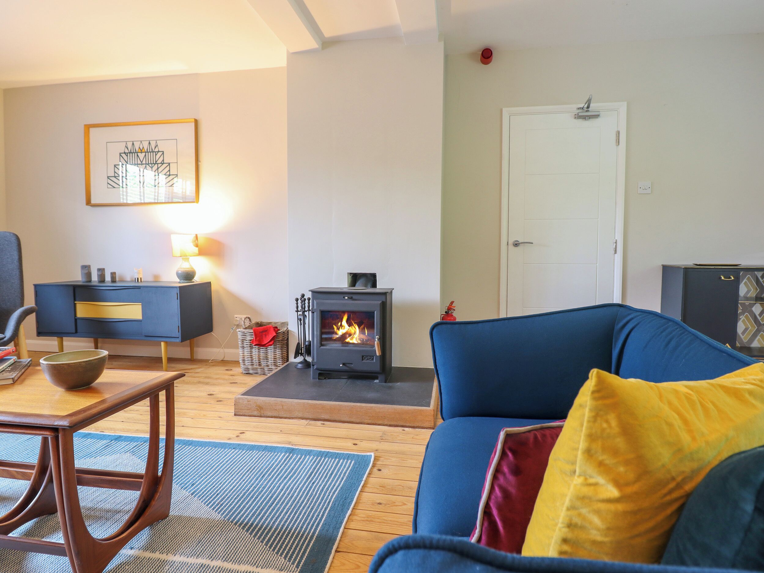 A living room with a blue sofa, a small table with a bowl, a fireplace, a dark blue cabinet, and a framed picture on the wall.
