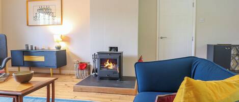 A living room with a blue sofa, a small table with a bowl, a fireplace, a dark blue cabinet, and a framed picture on the wall.