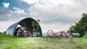 A green agricultural structure with a tractor and farming equipment nearby. - Agriturismo Prisma: Single Room with Private Bathroom (Villa Vergano)