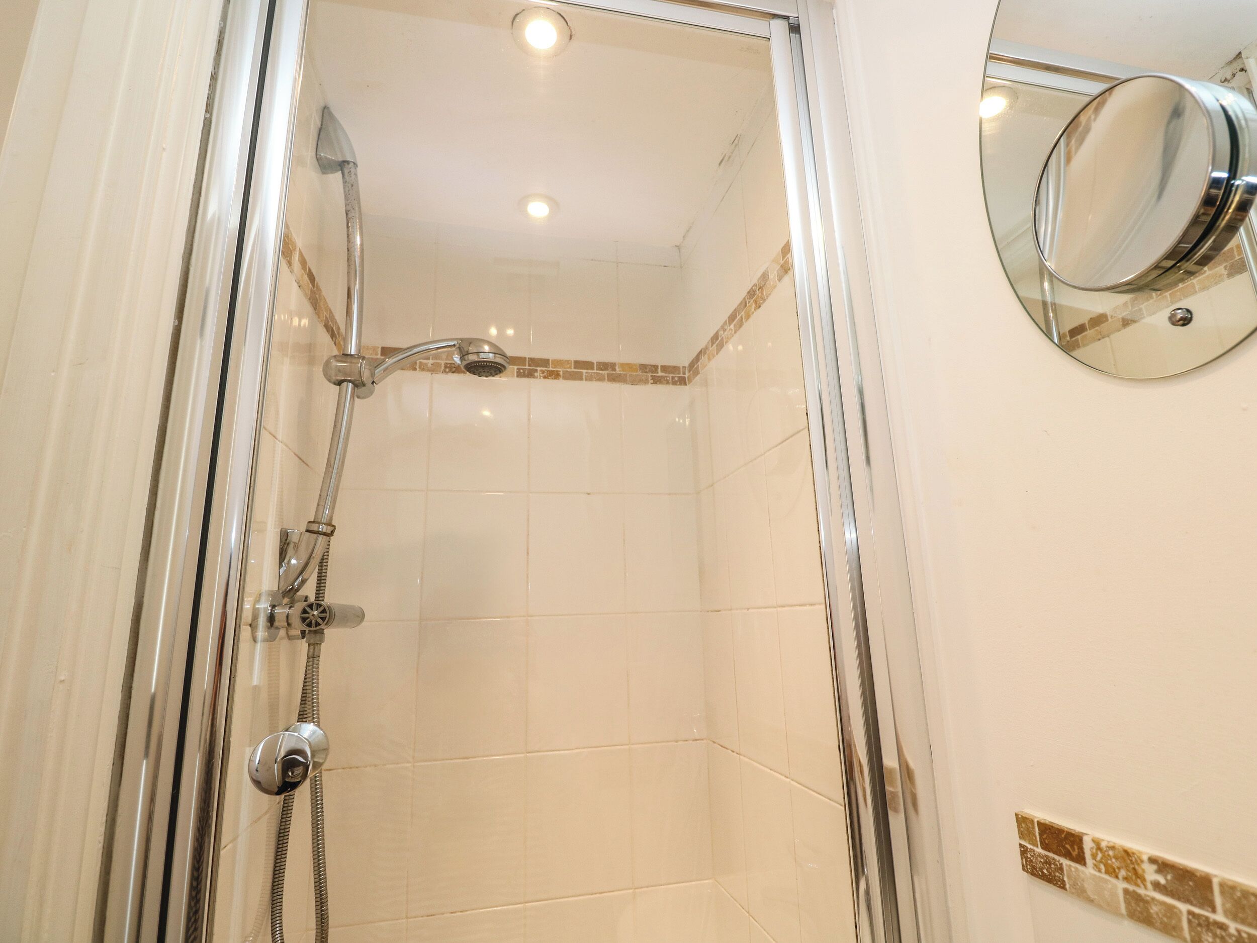 A glass-enclosed shower with a chrome showerhead and handheld shower attachment.