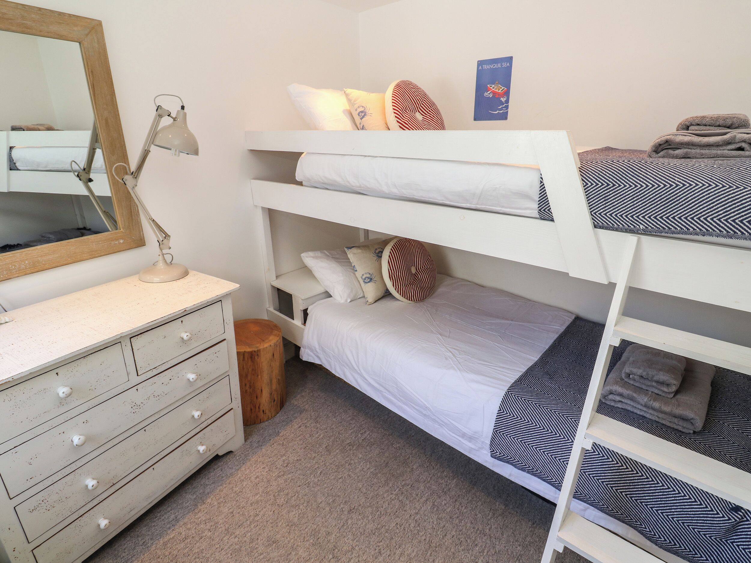 A bunk bed room with a dresser, a mirror, and a wall-mounted book titled "A Tranquil Sea".