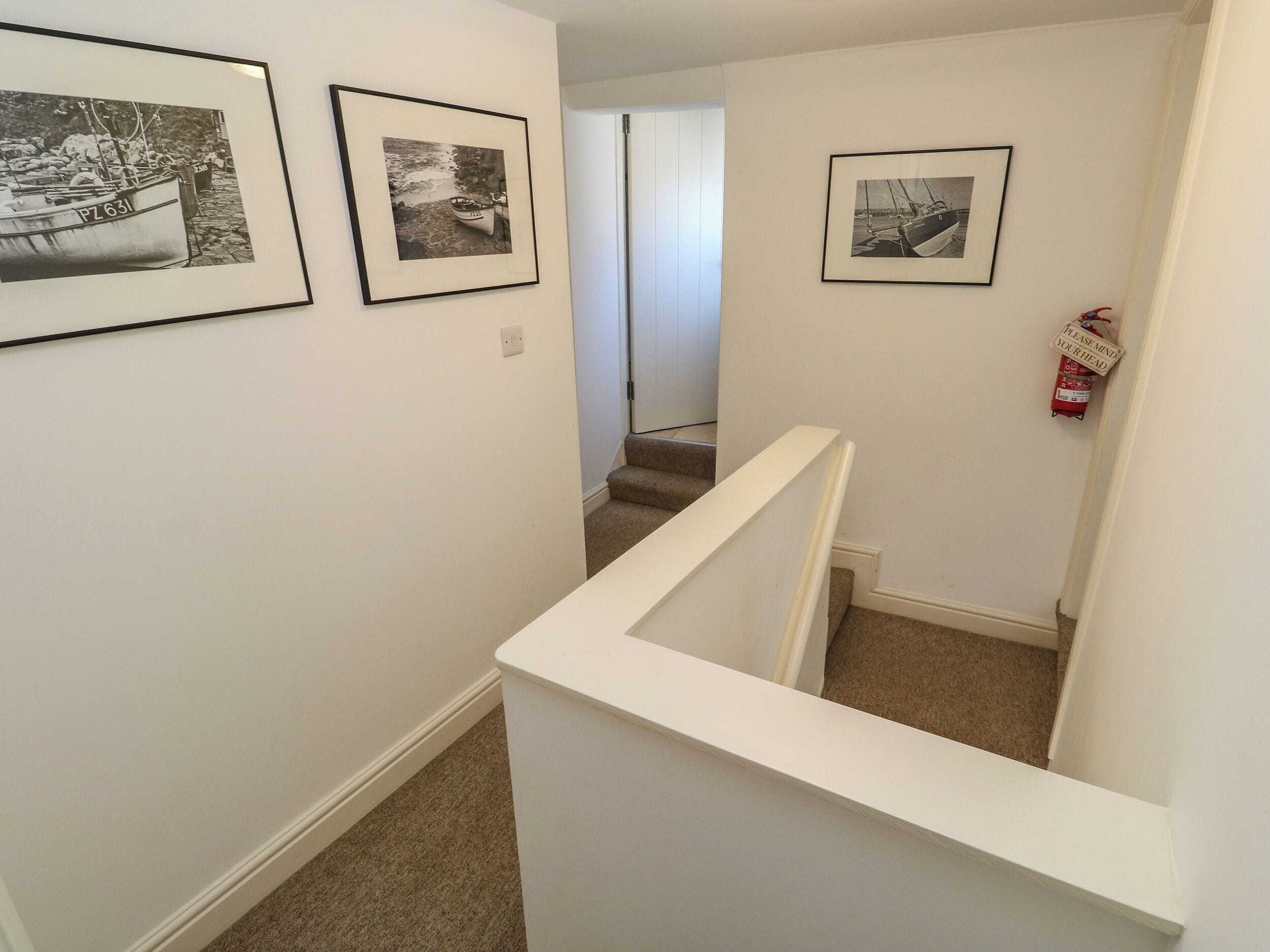 A staircase with a white railing, leading to a landing with three black and white photographs of boats on the wall.