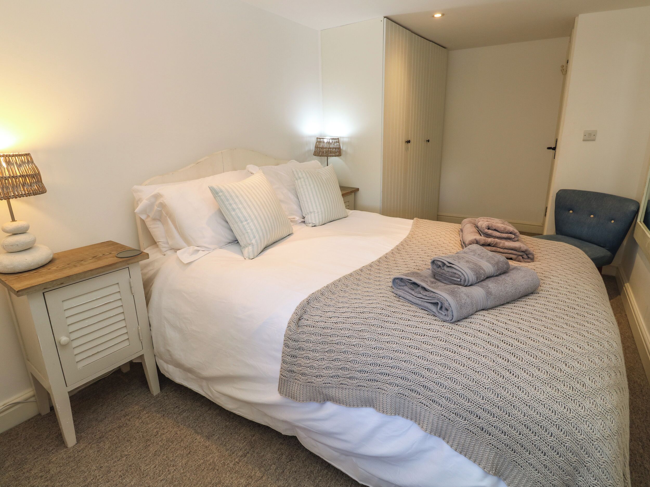 A neatly made bed with pillows, a bedside lamp, and folded towels.