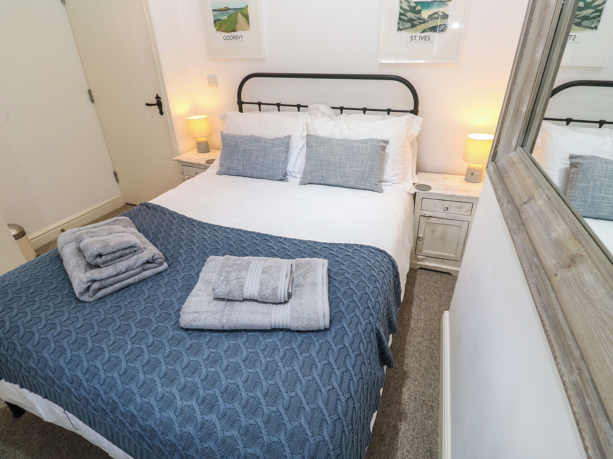 A neatly made bed with a blue patterned bedspread, two pillows, and folded towels on the side.