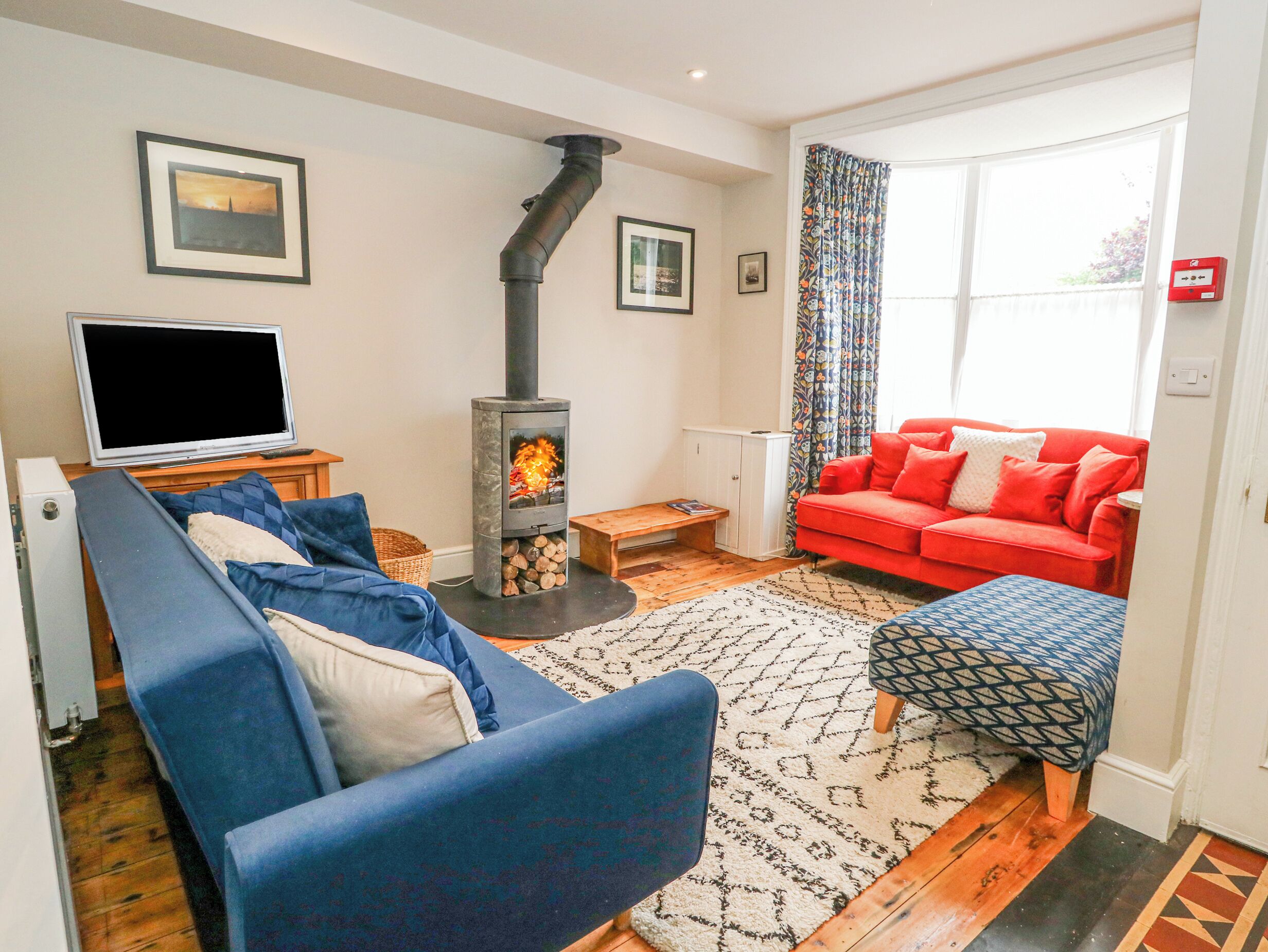 A living room with a sofa, a red couch, a television, a fireplace, and a window with curtains.