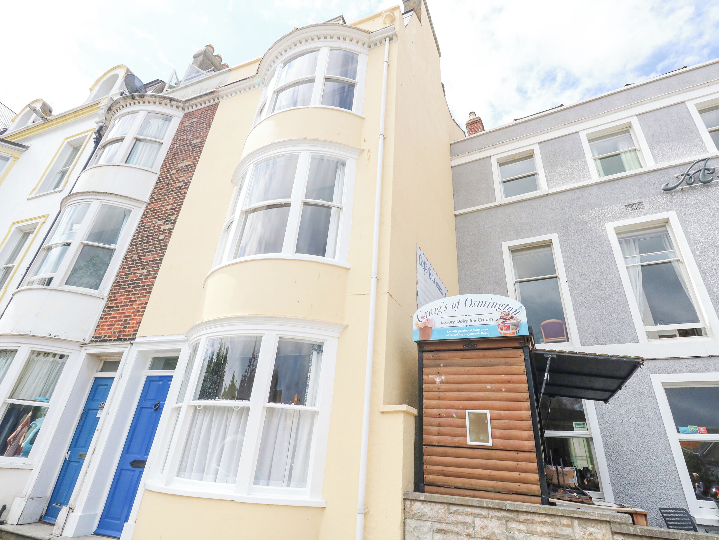 Un immeuble à plusieurs étages, doté d’une façade de couleur crème, de portes bleues et d’une enseigne indiquant « Craig’s of Osmington », un magasin de crème glacée artisanale.