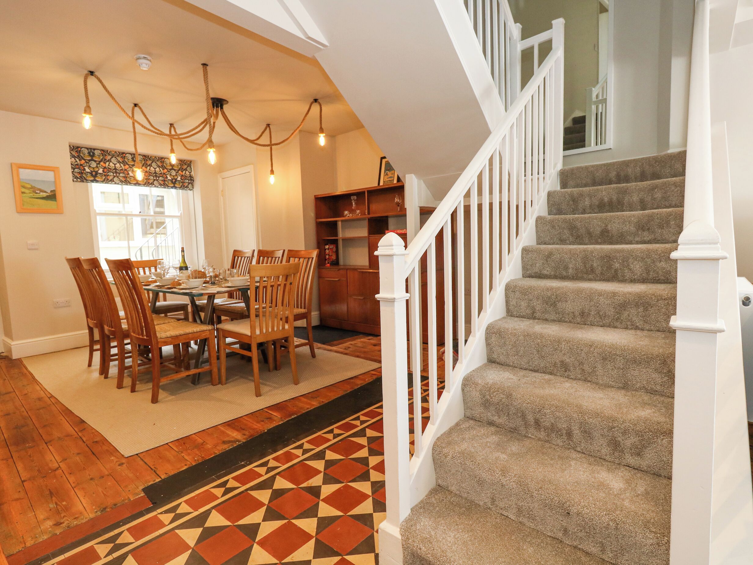 A dining area with a wooden table and chairs, a patterned rug, and a staircase with a white railing.