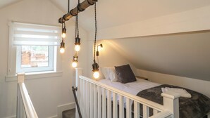 Une chambre avec un plafond en pente, une fenêtre avec des stores, un lit avec des oreillers et un luminaire suspendu.