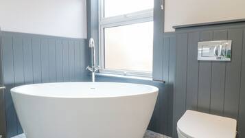 Un baño con bañera independiente, inodoro y ventana.