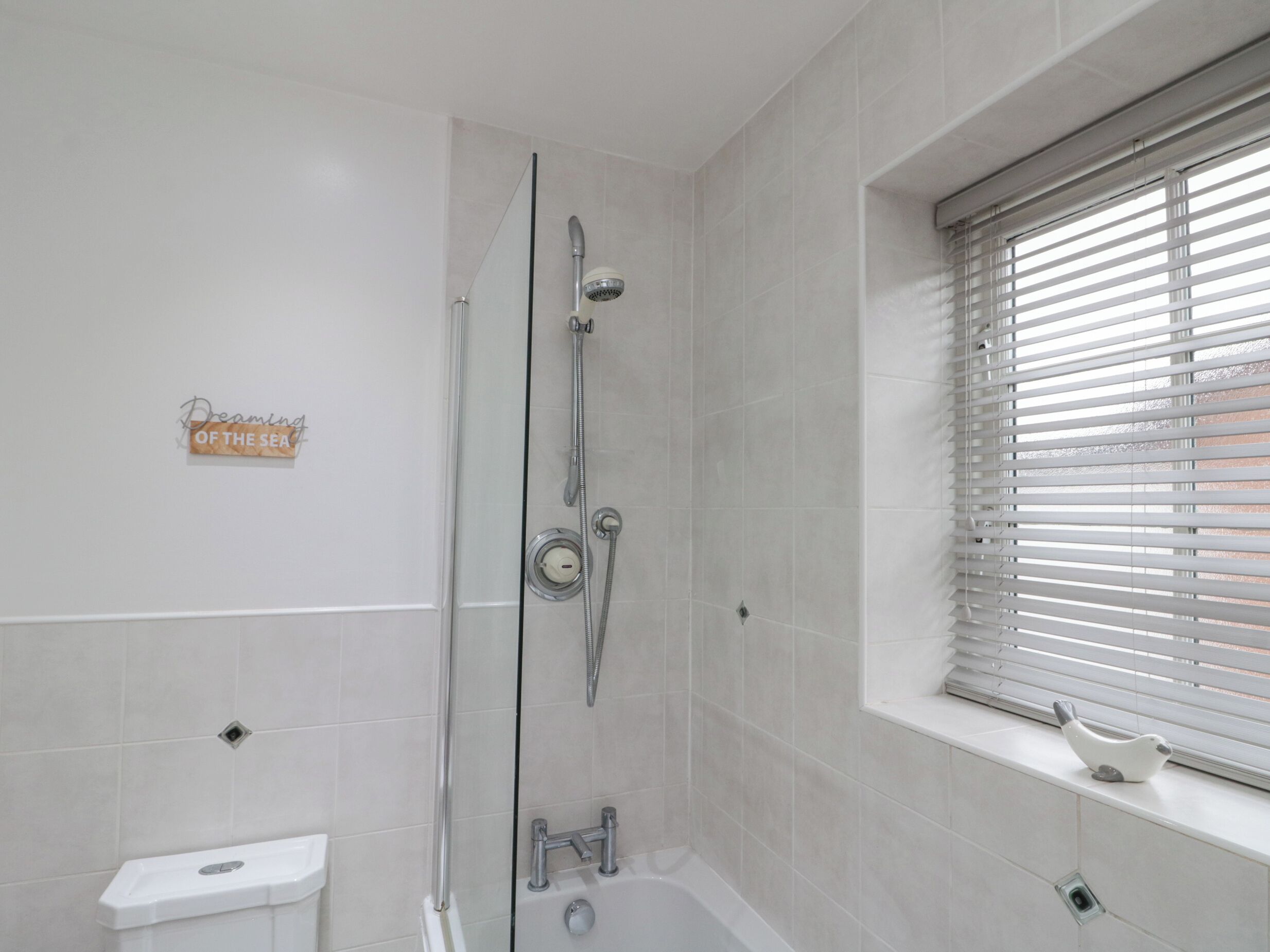Une salle de bain avec une douche à parois de verre, des toilettes et une fenêtre équipée de stores.