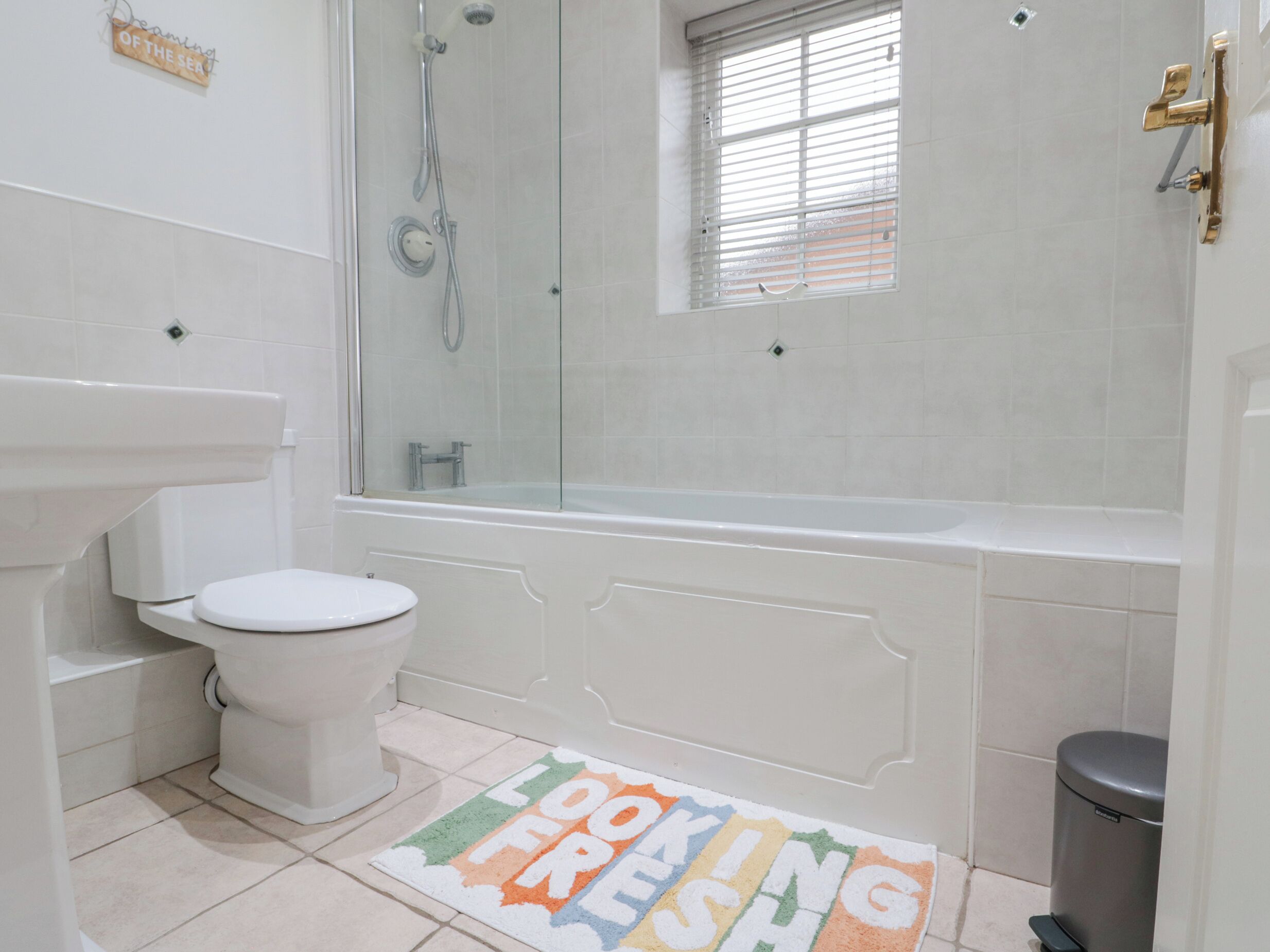 A bathroom with a toilet, sink, shower, and a window.