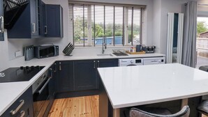 Een moderne keuken met donkere kastjes, een wit aanrecht, een ingebouwde oven, een magnetron en een raam met zonwering.