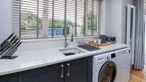 Een moderne keuken met een ingebouwde wasmachine, een spoelbak en een raam met zonwering.