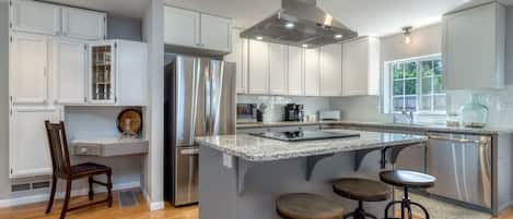 Una cocina moderna con armarios blancos, electrodomésticos de acero inoxidable y una isla central con taburetes de bar.