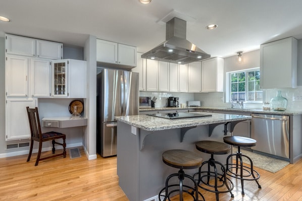A modern kitchen with white cabinetry, stainless steel appliances, and a central island with bar stools.