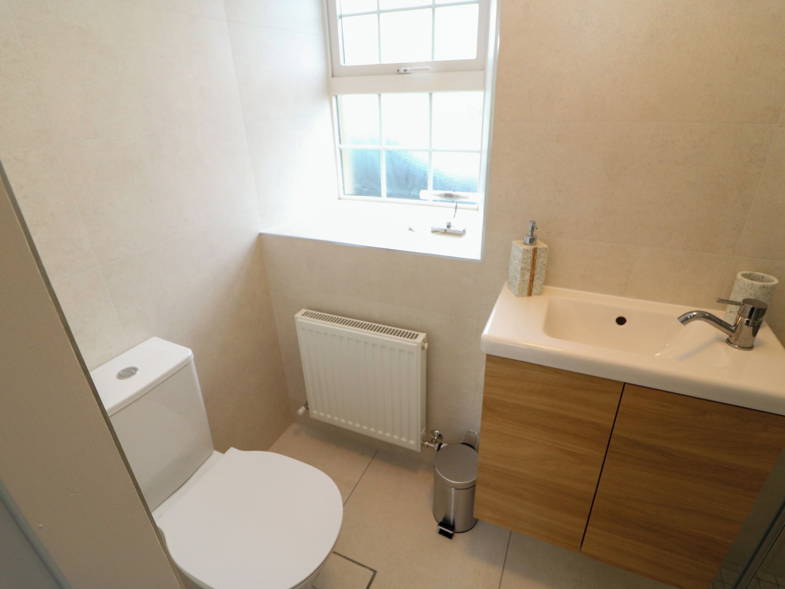 A small bathroom with a toilet, a radiator, a window, and a sink with a mirror.