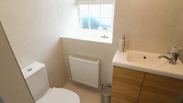 A small bathroom with a toilet, a radiator, a window, and a sink with a mirror.