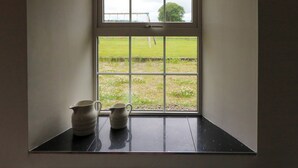 A window with a view of a grassy field and a tree. There are two ceramic pitchers on a black surface below the window. - Glebe Farmhouse (Killarney)