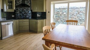 A kitchen with wooden cabinets, a built-in stove, and a dining area with a wooden table and chairs. - Glebe Farmhouse (Killarney)