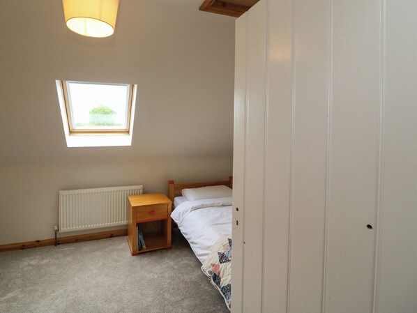 Une petite chambre avec un lit simple, une fenêtre, un radiateur et une table de chevet en bois.