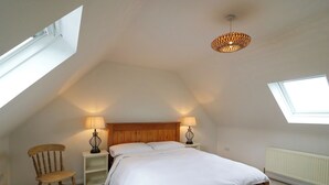A bedroom with a sloped ceiling, a wooden bed, two bedside lamps, a wooden chair, and a skylight. - Glebe Farmhouse (Killarney)