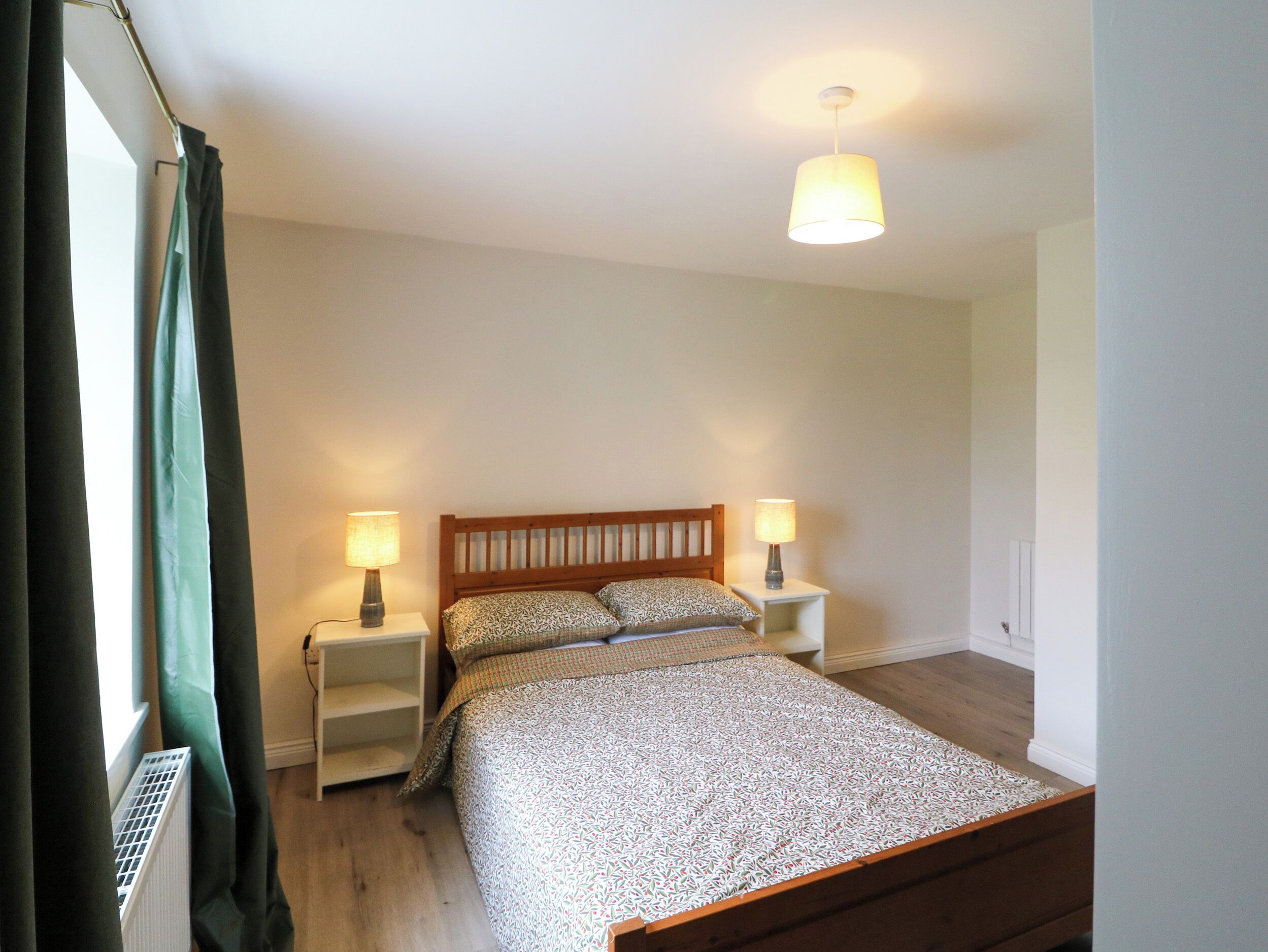 Een slaapkamer met een houten bed, twee bedlampen, een raam met gordijnen en een plafondlamp.