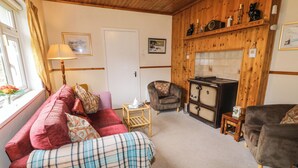 A cozy living room with a red sofa, a plaid blanket, a wooden cabinet, and a fireplace. - James Neills Cottage (Maghernalaght)