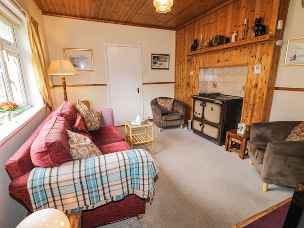 A cozy living room with a red sofa, a plaid blanket, a wooden cabinet, and a fireplace. - James Neills Cottage (Maghernalaght)