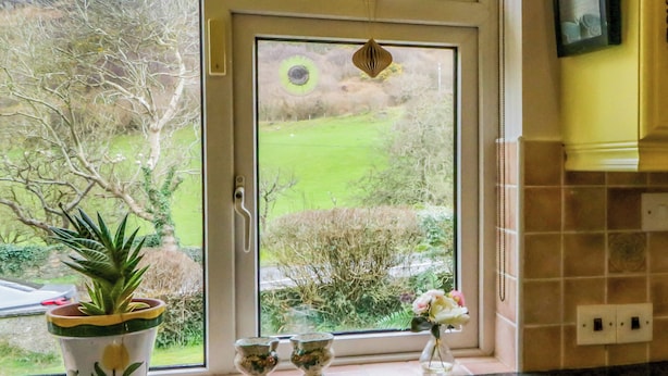 A kitchen with a window overlooking a green landscape. - James Neills Cottage (Maghernalaght)